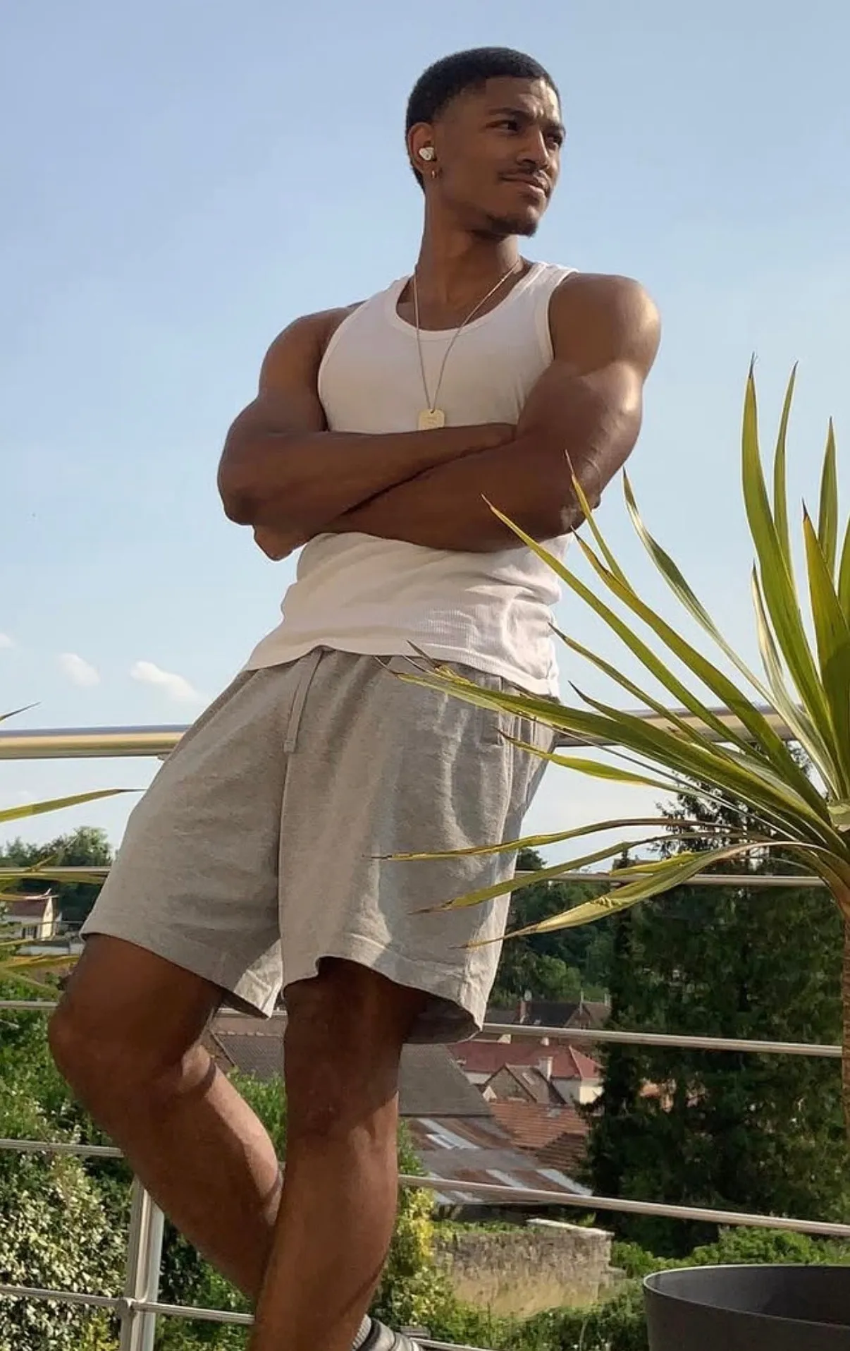Niels Montabord bras croisés, en débardeur blanc et short gris, sur une terrasse en plein soleil